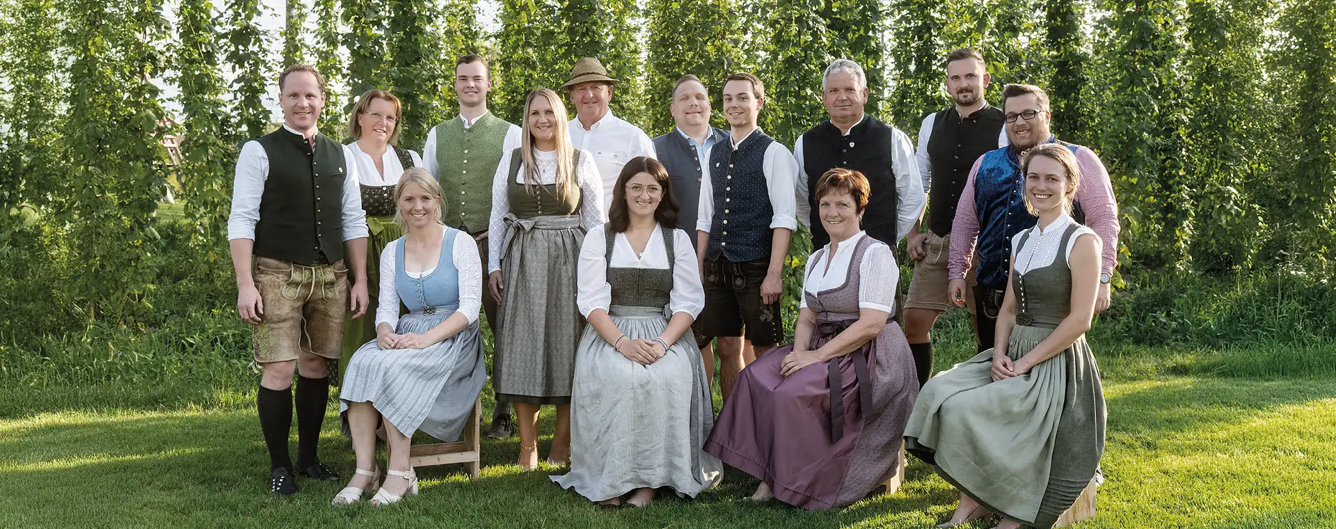 Das IGN-Team: 14 Frauen und Männer stehen in bayerscher Tracht als Gruppe in einem Hopfengarten und lächeln freundlich in die Kamera